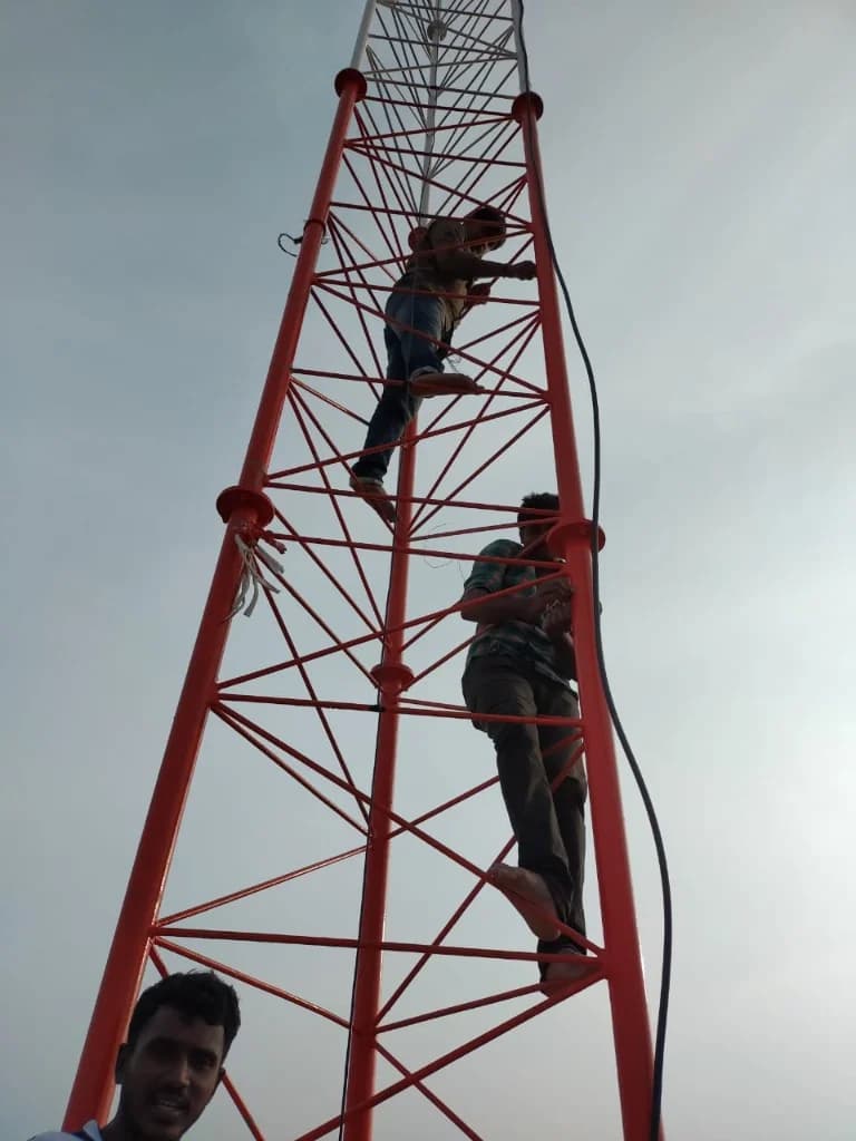 Technicians installing equipment on an orange broadcast tower lattice